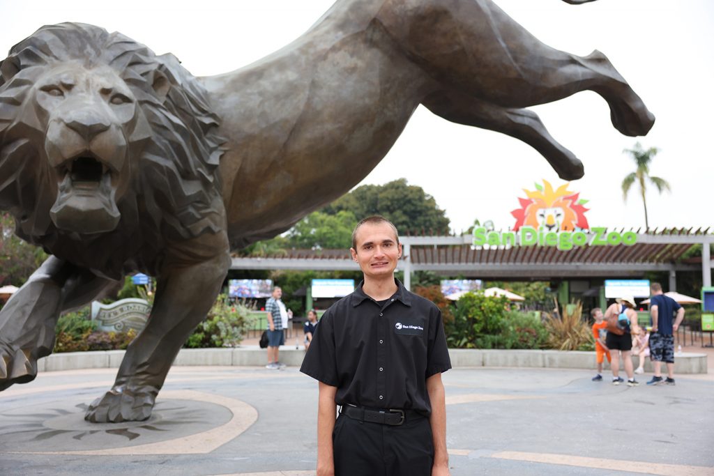 man wearing san diego zoo shirt standing in front of lion statue