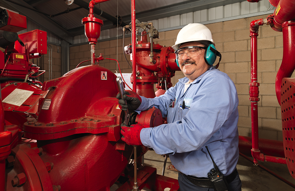 A man in safety glasses hard hat and ear muffs working on red metal pipes