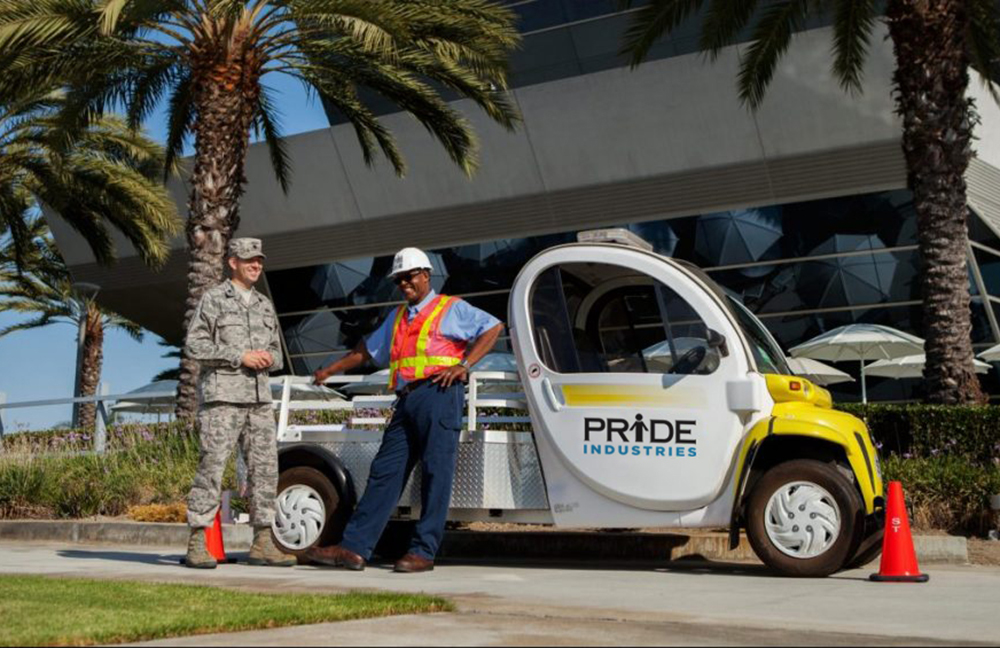 two men standing in front of golf cart with pride industries logo on it