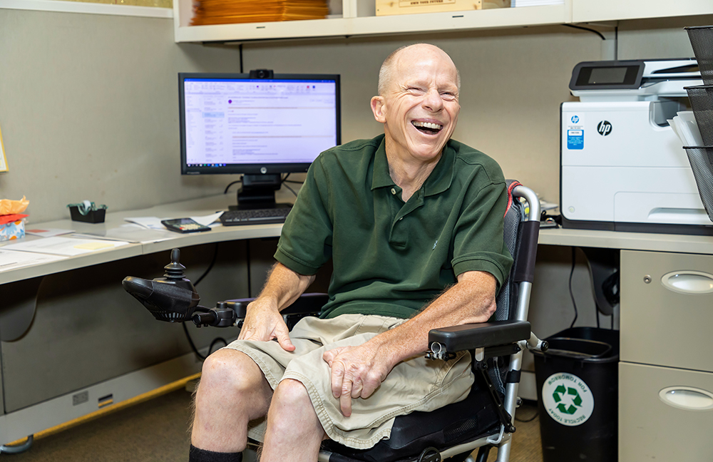 image of man in green shirt sitting in wheelchair in front of computer smiling