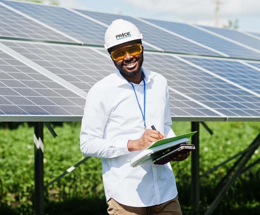 man wearing hard hat and safety glasses holding clipboard standing in front of solar panels
