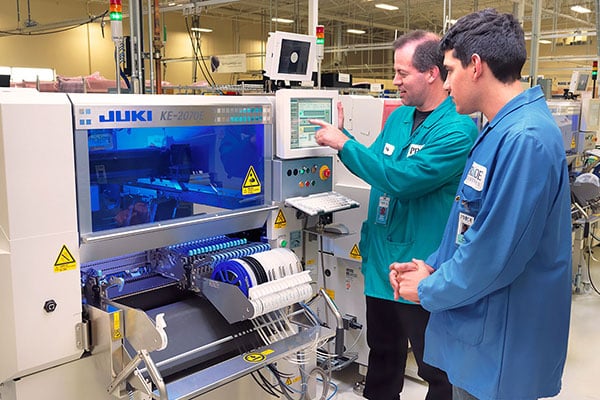 Two employees in blue coats working on manufacturing floor machine