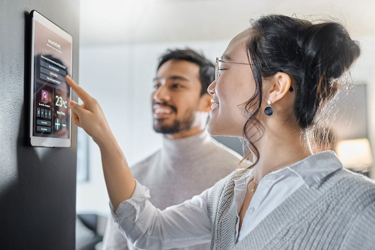 Two people in a living room, using their wall-mounted smart home interface