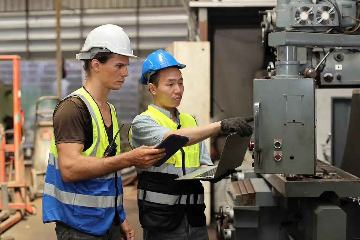 Two technicians, one holding a laptop and the other holding a tablet, standing at a piece of machinery in an industrial facility