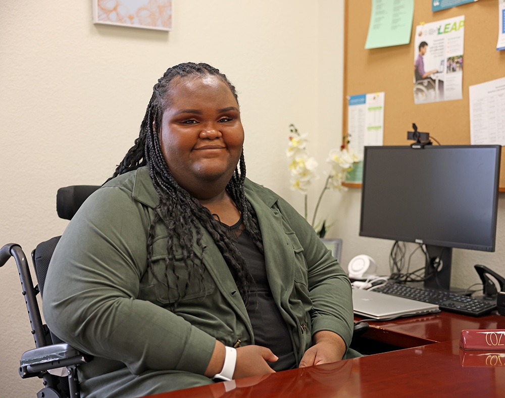Young African American woman in wheelchair sitting at desk smiling