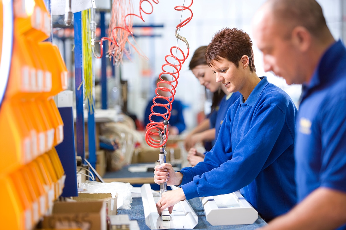 Four manufacturing technicians, wearing blue shirts, at a workstation building electronics devices