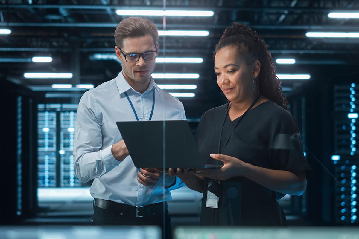 Two engineers, a man in glasses and a woman with long hair, looking at a laptop computer in an engineering lab