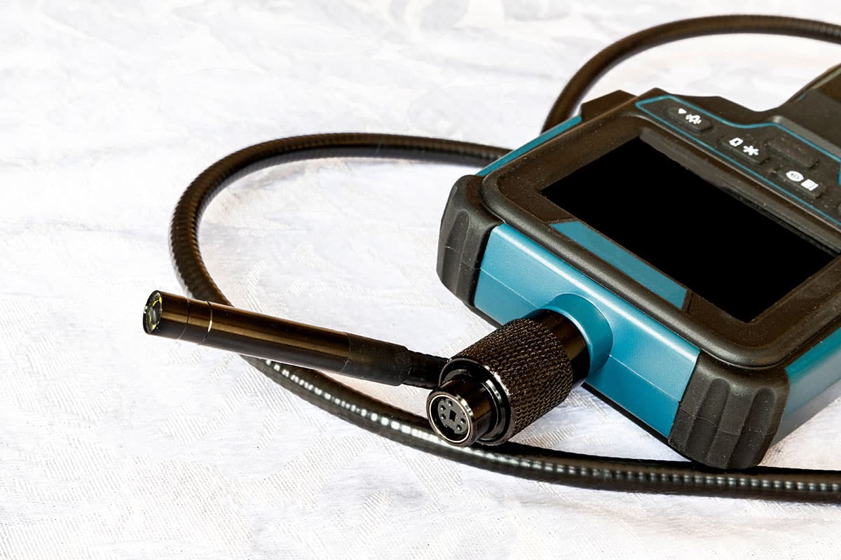 A close-up of a borescope, showing its long, flexible rod and display screen