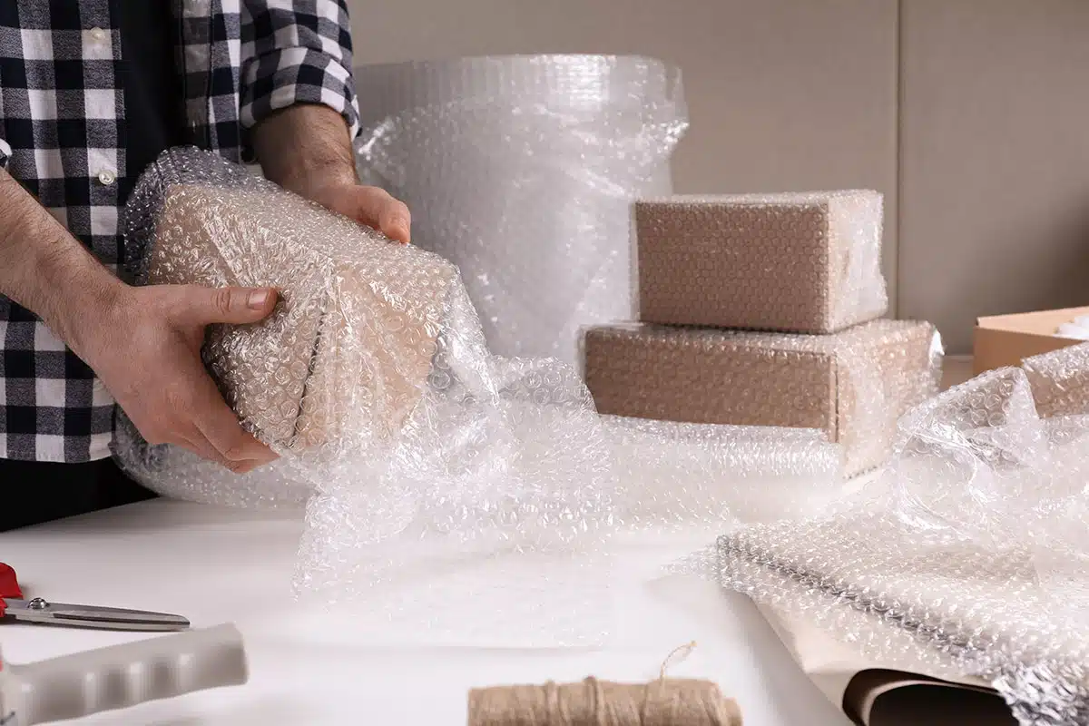 A man using plastic bubble wrap to cover a small cardboard box.