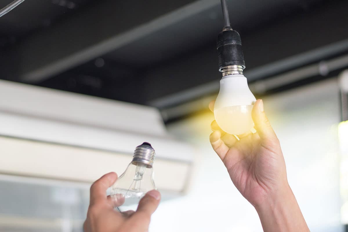 A close-up of two hands changing the bulb of an overhead fixture in a commercial facility