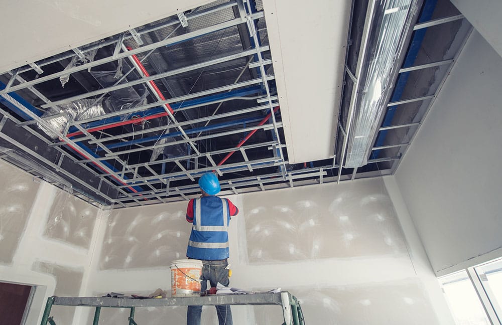 Construction worker in blue hardhat and vest working on office building ceiling