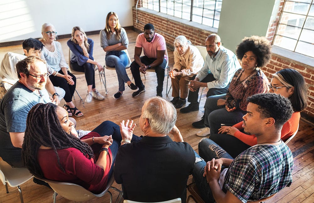A group of diverse people sit in circle talking
